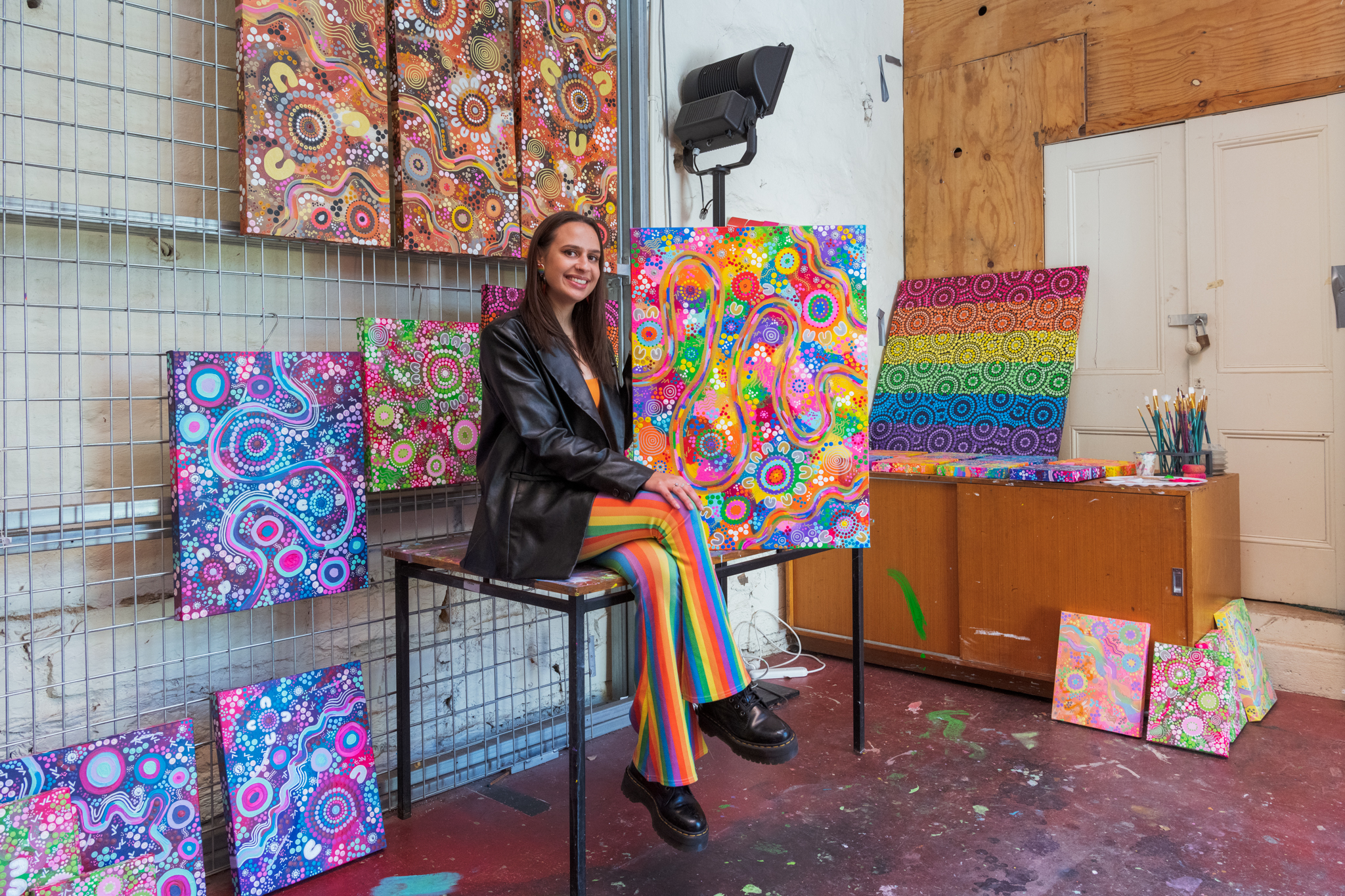 Mali Isabel sits on a table surrounded by her artwork