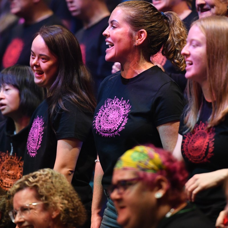 A choir wearing black t-shirts sing towards an audience