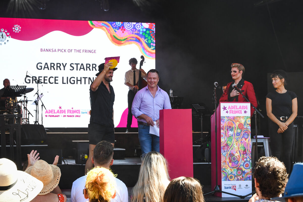 garry starr standing on stage with presenters, holding an award above is head in celebration of winning