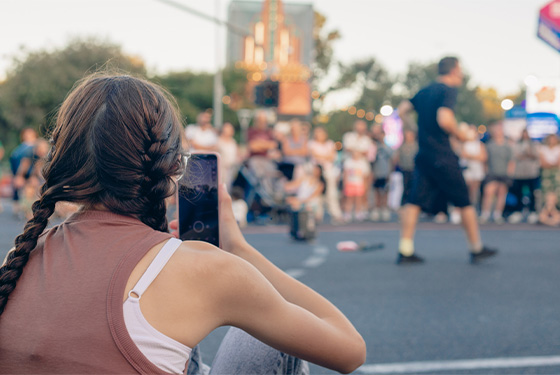A lady holds her phone whilst recording a street performer. 