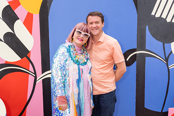 Adelaide Fringe CEO Heather Croall and Andy Beecroft standing in front of Fringe 2023 Poster backdrop. 