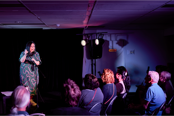 Comedian Jennifer Wong stand on stage performing to an audience. 