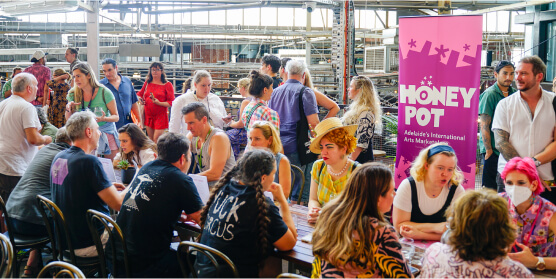groups of people lining up across a table talking to one another in a speed-dating style. A large pink banner saying 'Honey Pot' sits behind them