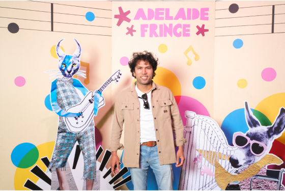 A photo of artist CJ stands in front on a backdrop that says Adelaide Fringe. 