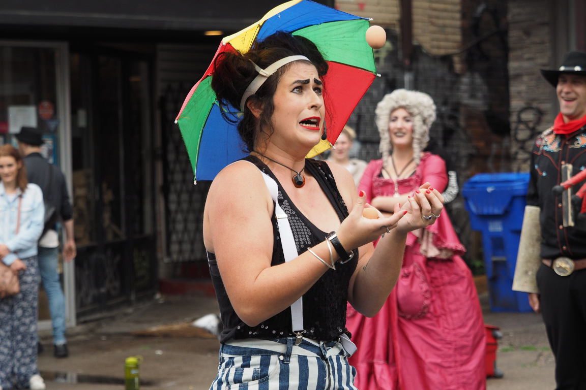 Women wearing a rainbow umbrella head juggling balls