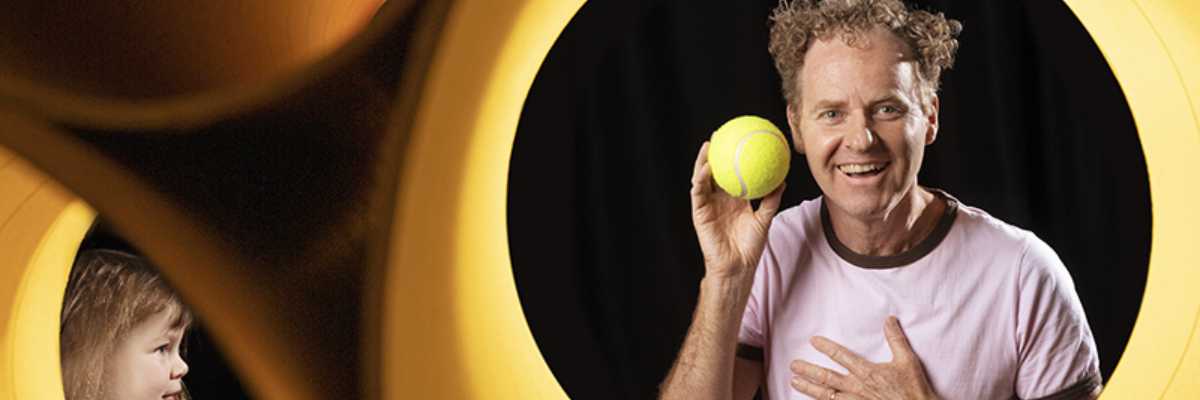 Man holding a tennis ball inside a giant yellow egg shaped object