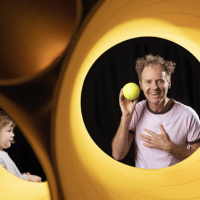 Man holding a tennis ball inside a giant yellow egg shaped object