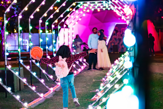 Child with open arms runs through a sparkling light tunnel at night, with two smiling adults watching from the end.