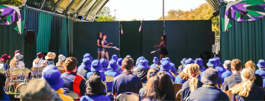 circus performers on stage in front of an audience of school children all wearing hats and uniforms