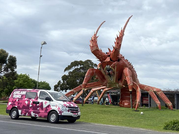 White, pink and purple branded Adelaide Fringe van parked on the side of the road next to Larry the Lobster, a large fake lobster.