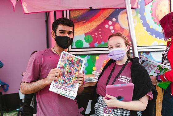 Adelaide Fringe volunteers standing at an information booth holding the Official Fringe Guide.