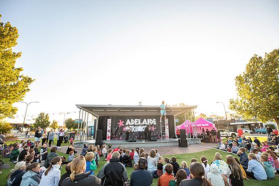 A stage with the Adelaide Fringe logo, large patch of grass in front with children running around