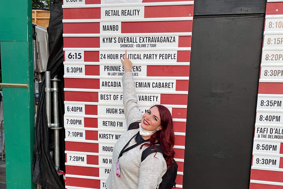 A lady with red hair stands in front of a wall pointing to the words that read 'Retail Reality.' 