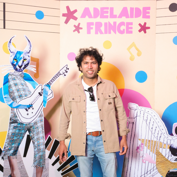 A photo of artist CJ stands in front of a sign that says Adelaide Fringe. 