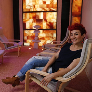 Woman wearing jeans and a black top sitting on a chair smiling at the camera