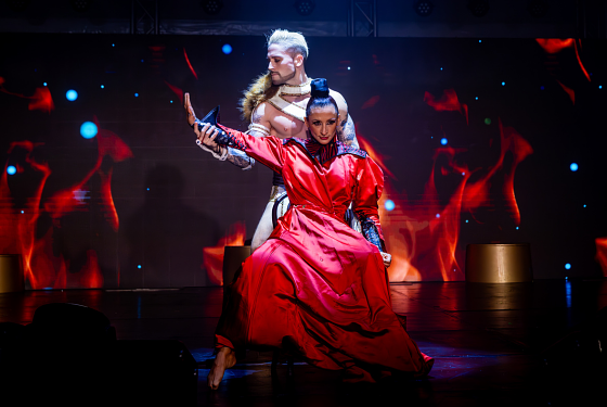 Two Zirque La La performers on a stage with red lights behind them. They dance in an embrace. 